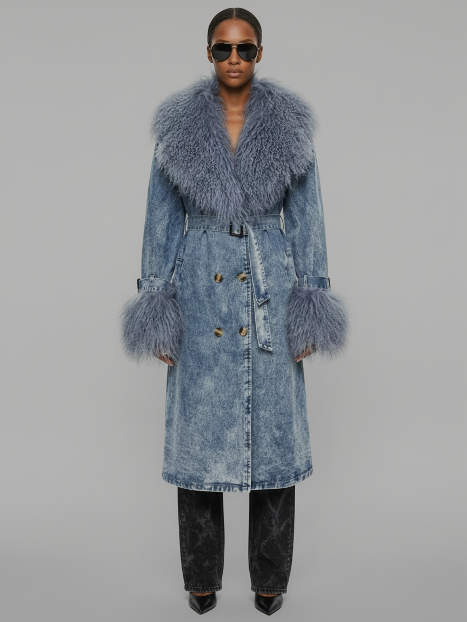 Woman wearing the Azure Shearling Denim Trench, acid-wash denim coat with real Mongolian fur collar and cuffs, double-breasted closure and waist belt.