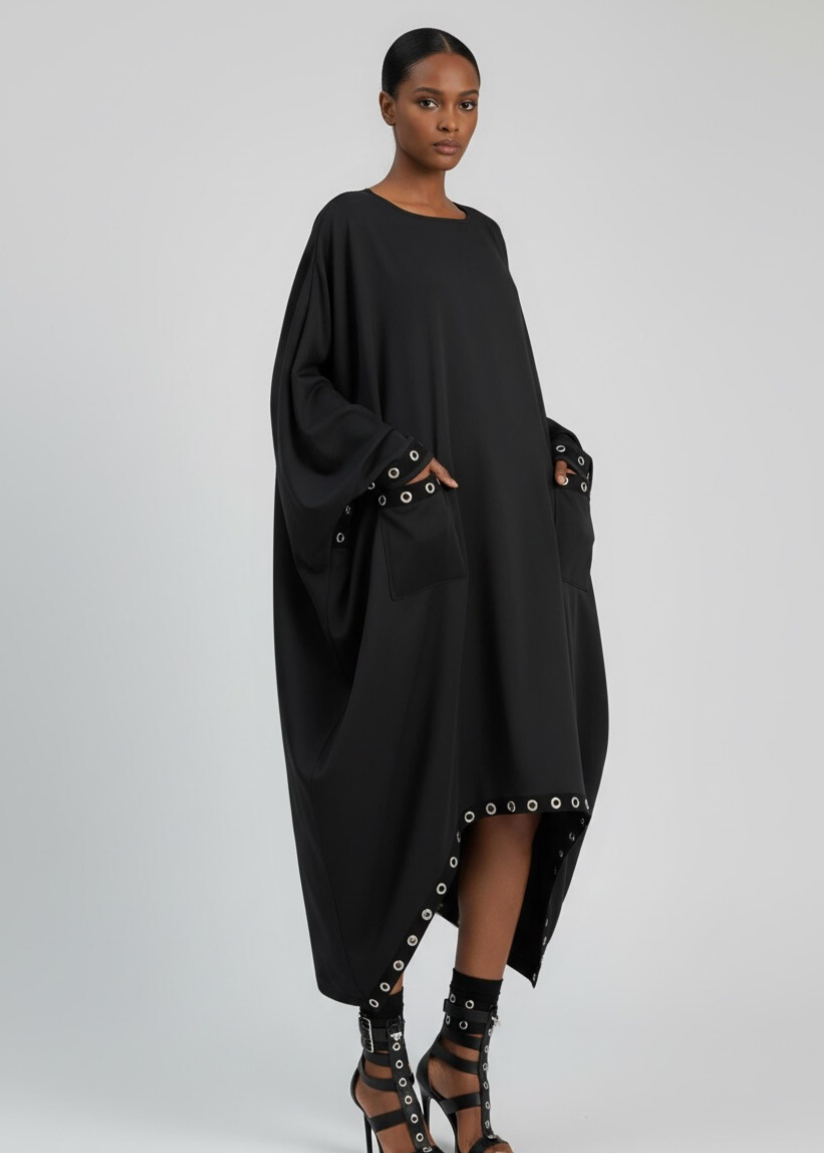 Draped oversized black dress with boat neckline and grommet-trim pockets.