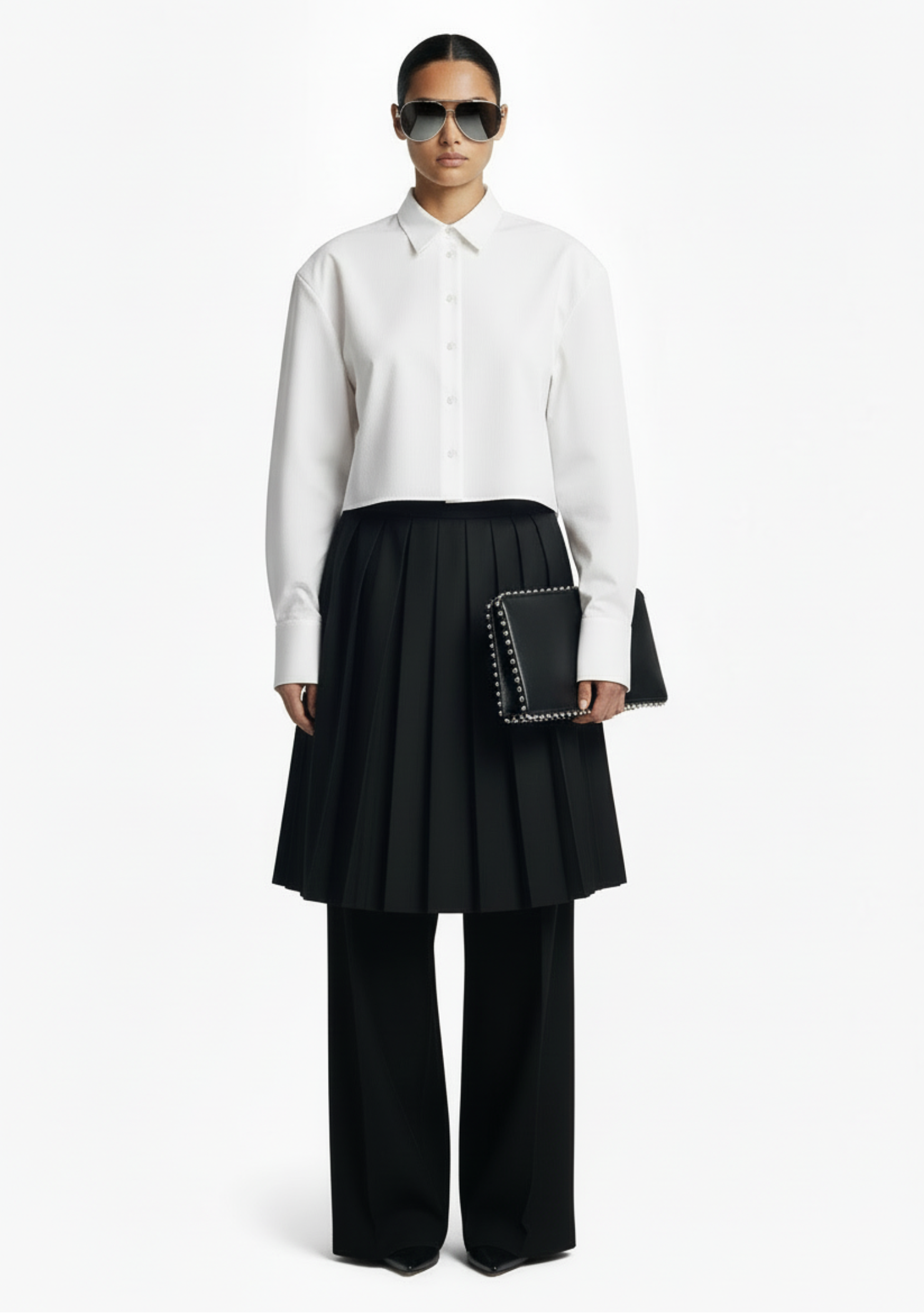 GOLD x TEAL Monarch Pleat Trousers shown on model in black wide-leg silhouette with detachable pleated skirt overlay, styled with a white shirt.