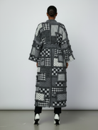 GOLDxTEAL Back view of the Noir Mosaic Duster featuring the full-length patchwork design and thick textured knit pattern in black, white, and grey.