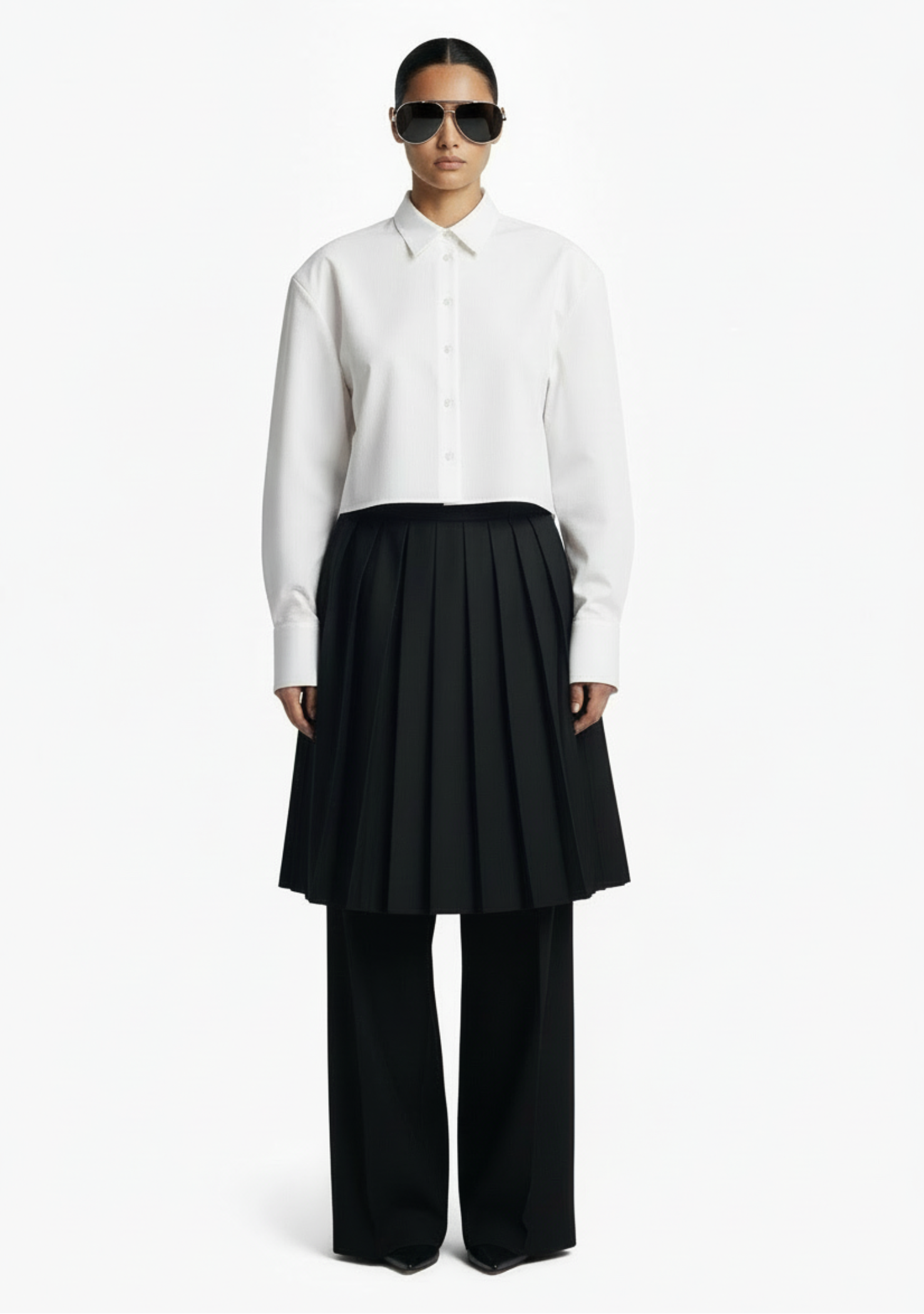 GOLD x TEAL Monarch Pleat Trousers shown on model in black wide-leg silhouette with detachable pleated skirt overlay, styled with a white shirt.